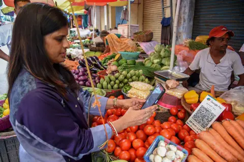 Một người phụ nữ quét mã QR sau khi mua rau tại chợ ở Kolkata